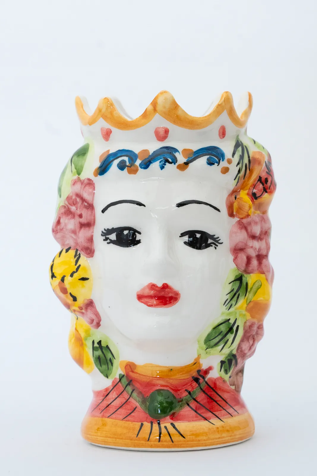 Vaso di ceramica colorata a forma di testa di donna, con corona, labbra rosse, sopracciglia dipinte ed elementi decorativi colorati, tra cui fiori e foglie. Il design è vivace con sfumature di giallo, rosa, verde e blu.