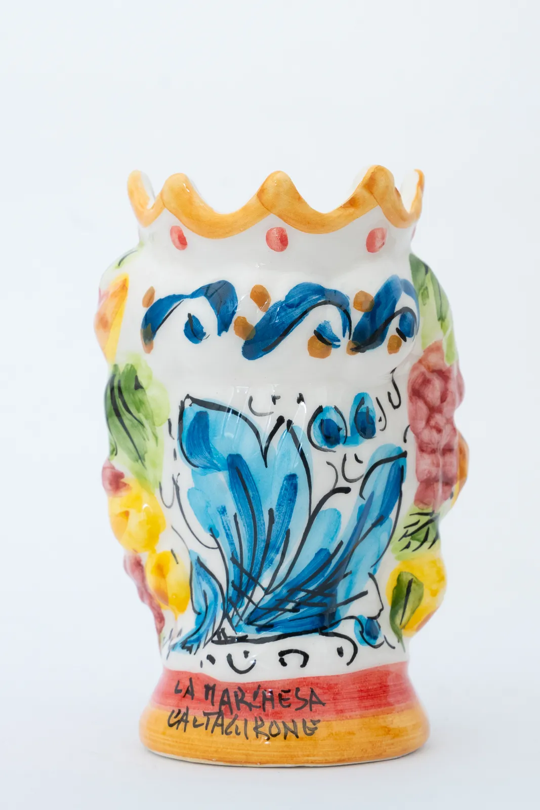 Un vaso di ceramica colorato e fatto a mano con intricati motivi floreali blu e accenti multicolori, caratterizzato da una parte superiore decorativa a forma di corona. La base è incisa con la scritta "La Marchesa Caltagirone.