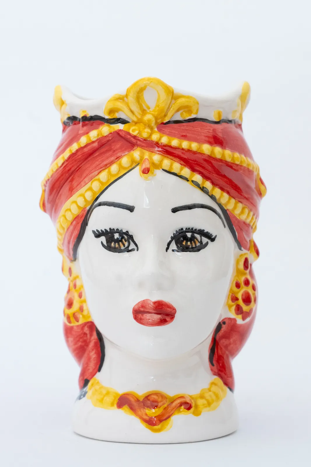 Busto in ceramica di una donna con foulard rosso e giallo, lineamenti del viso dettagliati e orecchini stilizzati. Il pezzo è colorato in modo brillante su uno sfondo bianco semplice.